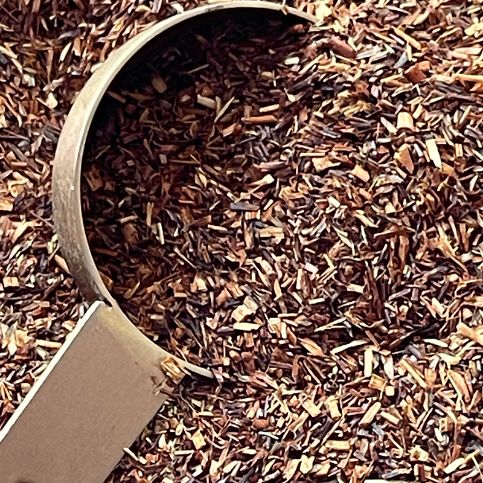 Naturally fermented Rooibos tea leaves displayed with a copper spoon, showcasing the rich colour and texture of the leaves